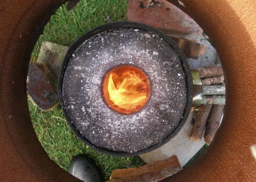 View of a home-made rocket stove from above, showing the insulation and the sticks feeding the flames.